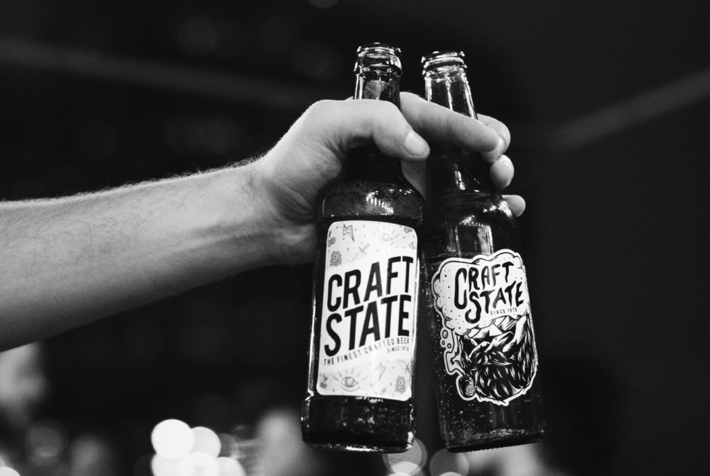 black and white picture of a hand holding two beer bottles with hand drawn labels